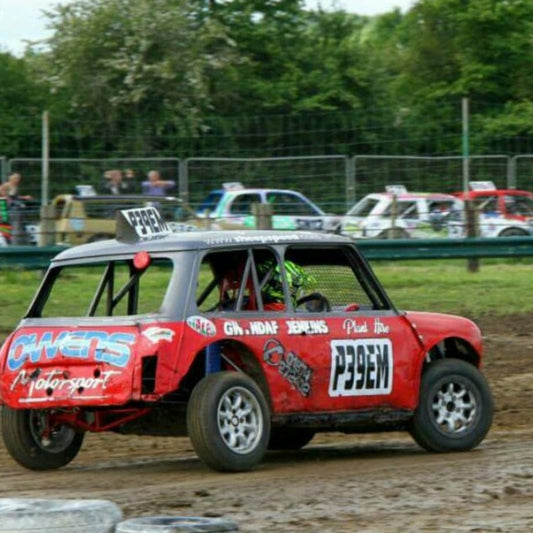 An autograss Mini race car leaning hard into a dirt track corner, showcasing chassis reliability under extreme lateral load.