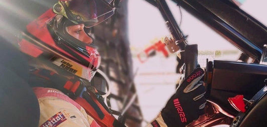 A female racing driver wearing a full-face helmet and fire-resistant overalls sits inside  her racing car