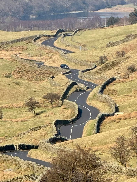 A winding asphalt road curves sharply through a dramatic mountain pass beneath a stormy grey sky.